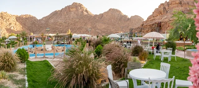 تجربة تجمع بين الراحة والهدوء والطبيعة في أحد مواقع ومعالم السياحة فى مدينة حائل بالمملكة العربية السعودية، منطقة جلوس خارجية في مقهى بقرية عقدة، طابع ريفي وسط الجبال وأشجار النخيل، نسيم الجبال البارد