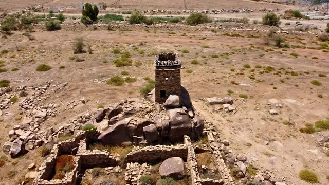 أطلال برج حجري قديم في قرية آل ينفع التراثية  في مركز تمنية في منطقة عسير في السعودية في وقت النهار، الاهتمام بزراعة النباتات و الأشجار الخضراء في إحدى القرى التراثية، الفن الهندسي المعماري للمعالم و الأماكن الأثرية القديمة في المدن التاريخيه