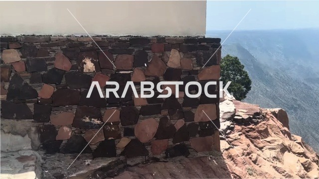 The peaks and mountain heights, a stone wall built in the traditional style on a deep valley, Al-Habla Park, famous tourist attractions in the Kingdom, buildings constructed from stones and tree trunks, the heritage architectural design of the village houses.