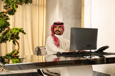النظر الى شيء ما، جذب واستقطاب المزيد من العملاء، العمل على زيادة مستوى رضا العميل، الإجابة عن الاستعلامات والاستفسارات, رجل عربي خليجي سعودي يرتدي الثوب الابيض و الشماغ يعمل على جهاز الحاسوب