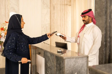 استخدام الوسائل والتقنيات الحديثة في الدفع الالكتروني, امراه عربيه خليجيه سعودية ترتدي العباءة و الحجاب تمسك بيديها حقيب السفرفي إحدى الفنادق الفاخرة, سهولة الدفع الالي في السعودية, التحكم بالحجوزات والدفع من خلال الجوال, الاستمتاع بقضاء وقت ممتع