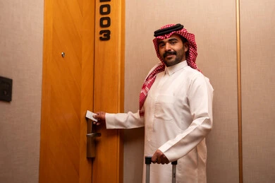 فتح الغرفة باستخدام البطاقة الإلكترونية، الاستمتاع بالعطله السياحيه، قفل متطور وحديث في فندق راقي، رجل عربي خليجي سعودي يرتدي الثوب الابيض و الشماغ يمسك بيدية حقيبة السفر يقوم بفتح باب غرفة فندقية، السياحه في المملكه العربيه السعوديه