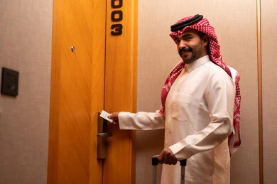 فتح الغرفة عبر كرت المفتاح، الاستمتاع بالعطله السياحيه، قفل متطور وحديث في فندق راقي، رجل عربي خليجي سعودي يرتدي الثوب الابيض و الشماغ يمسك بيدية حقيبة السفر يقوم بفتح باب غرفة فندقية، السياحه في المملكه العربيه السعوديه