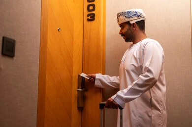 A modern and advanced lock in a luxury hotel, an Arab Gulf Omani man wearing a dishdasha and turban is opening the door to a hotel room, tourism in the Kingdom of Saudi Arabia, opening the door with an electronic card, enjoying tourist holidays and the summer vacation.