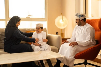 An Omani Gulf Arab family dressed in traditional attire sits in one of the upscale hotels, displaying gestures of happiness and joy, spending enjoyable times filled with love and affection, warmth and love between parents and children, the concept of safety and family stability.