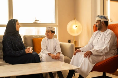 The intimacy and love between parents and children, the concept of safety and family stability, an Arab Gulf Omani family dressed in traditional attire sitting in one of the luxury hotels, spending enjoyable times filled with love and affection, gestures of happiness and joy.