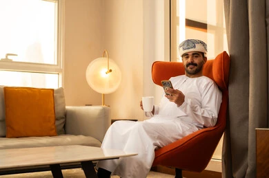 الاستمتاع بشرب المشروب المفضل، العمل عن بعد، استخدام جهاز تقني حديث ومتطور، تبادل الحديث والتواصل مع الأهل والأصدقاء، رجل عربي خليجي عماني يرتدي الدشداشة و الكمة يجلس داخل الفندق و يمسك بيده الهاتف المحمول، تصفح التطبيقات وبرامج التواصل الاجتماعي الاستمتاع بشرب المشروب المفضل، العمل عن بعد، استخدام جهاز تقني حديث ومتطور، تبادل الحديث والتواصل مع الأهل والأصدقاء، رجل عربي خليجي عماني يرتدي الدشداشة و الكمة يجلس داخل الفندق و يمسك بيده الهاتف المحمول، تصفح التطبيقات وبرامج التواصل الاجتماعي