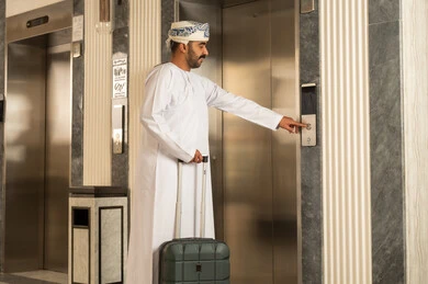 Preparing for the summer vacation, moving between floors by elevator, an Arab Gulf Omani man wearing a dishdasha and a turban is holding a suitcase in his hands while using the electric elevator.