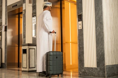 الانتقال بين الطوابق بالمصعد، رجل عربي خليجي عماني يرتدي الدشداشة و العمامة يمسك بيدية حقيبة السفر يقوم باستخدام المصعد الكهربائي ,  الاستعداد لقضاء الاجازه الصيفية