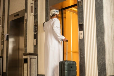 صعود ونزول الطوابق بالمصعد، رجل عربي خليجي عماني يرتدي الدشداشة و العمامة يمسك بيدية حقيبة السفر يقوم باستخدام المصعد الكهربائي ,  الاستعداد لقضاء الاجازه الصيفية