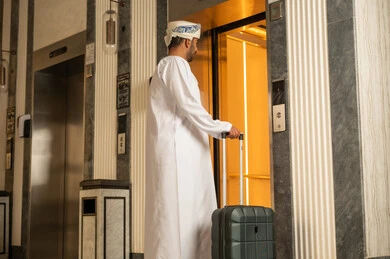 Using the elevator, an Arab Gulf Omani man wearing a dishdasha and a turban is holding a suitcase in his hands while using the elevator, preparing to spend the summer vacation.