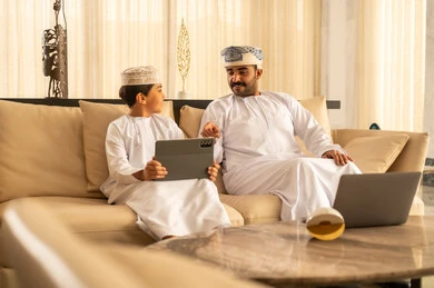 The concept of education through love and affection, sharing the reading of useful stories with children, watching movies and series on a tablet, an Arab Gulf Omani man wearing a dishdasha and turban sitting in the hotel lobby with his son, utilizing time to teach and raise children, using modern technological devices. The concept of education through love and affection, sharing the reading of useful stories with children, watching movies and series on a tablet, an Arab Gulf Omani man wearing a dishdasha and turban sitting in the hotel lobby with his son, utilizing time to teach and raise children, using modern technological devices.