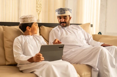 مشاهده الافلام و المسلسلات عبر جهاز التابلت ، المشاركه بقراءه القصص المفيده مع الأبناء، مفهوم التربيه بالحب والحنان، رجل عربي خليجي عماني يرتدي الدشداشة و العمامة يجلس في لوبي الفندق برفقه ابنه, استغلال الاوقات في تعليم وتربيه الاولاد، استخدام جهاز تقني حديث مشاهده الافلام و المسلسلات عبر جهاز التابلت ، المشاركه بقراءه القصص المفيده مع الأبناء، مفهوم التربيه بالحب والحنان، رجل عربي خليجي عماني يرتدي الدشداشة و العمامة يجلس في لوبي الفندق برفقه ابنه, استغلال الاوقات في تعليم وتربيه الاولاد، استخدام جهاز تقني حديث
