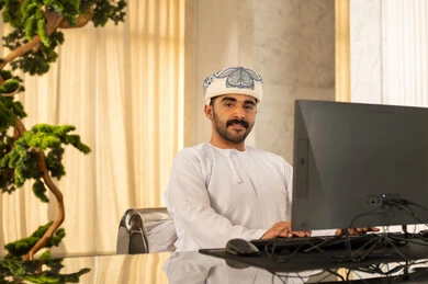 الإجابة عن الاستعلامات والاستفسارات، جذب واستقطاب المزيد من العملاء، العمل على زيادة مستوى رضا العميل, رجل عربي خليجي عماني يرتدي الدشداشة و العمامة يعمل على جهاز الحاسوب