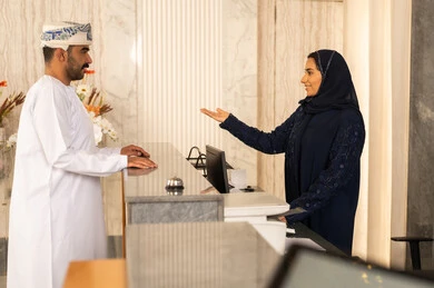 Welcoming guests and friendliness, the concept of tourism, hospitality, and travel, an Arab Gulf Omani man wearing a dishdasha and turban inquiring at customer service, booking a guest room through the reception. Welcoming guests and friendliness, the concept of tourism, hospitality, and travel, an Arab Gulf Omani man wearing a dishdasha and turban inquiring at customer service, booking a guest room through the reception.