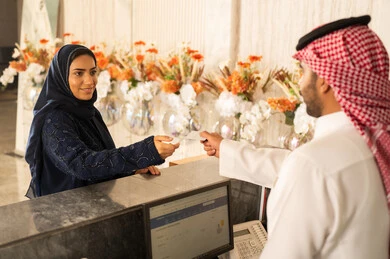 تسجيل حجز غرفة عند الاستقبال، ايماءات السرور والسعادة ، خدمة ومكتب إستقبال العملاء ، امراه عربيه خليجيه سعودية ترتدي العباءة و الحجاب تستلم بطاقة الغرفه