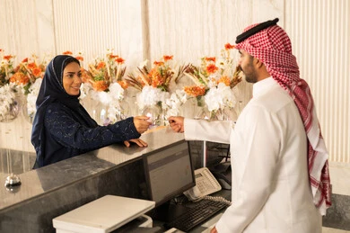 إجراء حجز فندقي عند الاستقبال، ايماءات السرور والسعادة ، خدمة ومكتب إستقبال العملاء ، امراه عربيه خليجيه سعودية ترتدي العباءة و الحجاب تستلم بطاقة الغرفه
