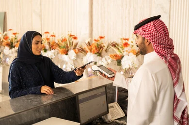 امراه عربيه خليجيه سعودية محجبة ترتدي العباءة و الحجاب تقوم بالدفع بطريقة الكترونية بإستخدام الهاتف المحمول في مكتب الاستقبال، إستعلامات وإستفسارات فى خدمة العملاء ،إجراءات الحجز والدخول لدى مكتب الاستقبال في الفندق، سياحه وفندقه وسفر