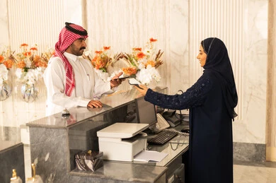تسجيل الدخول وإجراءات الاستقبال، استعلام و استفسار فى خدمة العملاء، سياحه وفندقه وسفر، رجل عربي خليجي سعودي يرتدي الثوب الابيض و الشماغ يقوم بالدفع عند الكاشير بطريقة الكترونية بإستخدام بطاقة الإئتمان البنكية