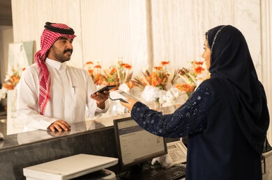إجراءات النزيل في الفندق، استعلام و استفسار فى خدمة العملاء، سياحه وفندقه وسفر، رجل عربي خليجي سعودي يرتدي الثوب الابيض و الشماغ يقوم بالدفع عند الكاشير بطريقة الكترونية بإستخدام بطاقة الإئتمان البنكية