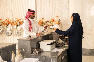 استعلام و استفسار فى خدمة العملاء، سياحه وفندقه وسفر، إجراءات الحجز والدخول لدى مكتب الاستقبال في الفندق، رجل عربي خليجي سعودي يرتدي الثوب الابيض و الشماغ يقوم بالدفع عند الكاشير بطريقة الكترونية بإستخدام بطاقة الإئتمان البنكية