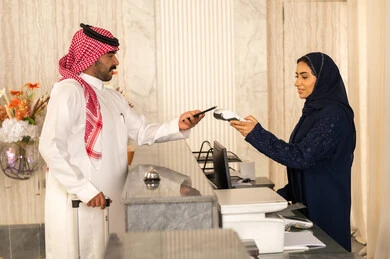 إجراءات الحجز والدخول لدى مكتب الاستقبال في الفندق، سياحه وفندقه وسفر، رجل عربي خليجي سعودي يرتدي الثوب الابيض و الشماغ يقوم بالدفع عند الكاشير بطريقة الكترونية بإستخدام بطاقة الإئتمان البنكية،إستعلامات وإستفسارات فى خدمة العملاء