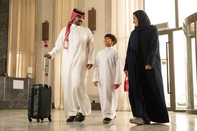 الاستعداد لقضاء رحلة سياحية ممتعه مع العائلة، الاستمتاع في قضاء الوقت مع الأهل, تبادل الاحاديث بتعابير السرور و السعادة, رجل عربي خليجي سعوجي يرتدي الثوب الابيض و الشماغ يمسك بيده حقيبة السفر برفقة زوجته و ابنه