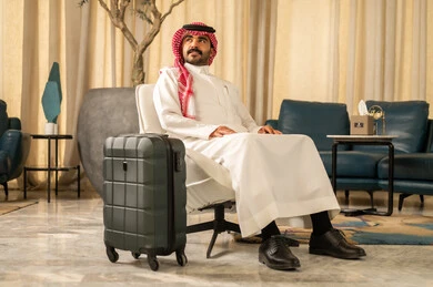 قضاء رحلة صيفية ممتعة، القيام بجولة ترفيهية، النظرالى شيء ما، مفهوم السياحة في إجازة الصيف، رجل عربي خليجي سعودي يرتدي الثوب الابيض و الشماغ يجلس بجانب حقيبة السفر ، السياحة في إجازة الصيف