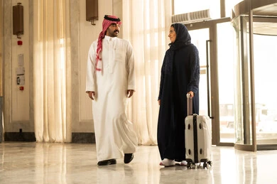 مفهوم السياحة في إجازة الصيف، امراه عربيه خليجيه سعودية محجبة ترتدي العباءة تمشي برفقة زوجها داخل الفندق و تمسك بيديها حقيبة السفر، تعابير وايماءات السعادة والسرور، قضاء وقت وقت ممتع، الاستعداد للسفر في جولة سياحية، قضاء رحلة صيفية مسلية