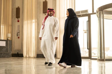 قضاء أجمل الأوقات في أفضل الفنادق الخليجية ، مفهوم الأسرة السعيدة، زوجان عربيان خليجيان سعوديان سائحان يرتديان الزي التقليدي يمشيان ويتجولان في بهو الفندق السياحي، رحلة زوجية ممتعة ، أجواء عائلية مرحة ، عطلة نهاية الأسبوع