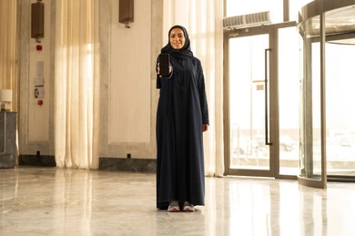 النظر إلى الكاميرا بتعابير السعادة والسرور، امرأة عربية خليجية سعودية محجبة ترتدي العباءة وتقف داخل فندق سياحي وتعرض شاشة سوداء فارغة عبر الهاتف المحمول، استخدام الجهاز والتقنية الحديثة والمتطورة النظر إلى الكاميرا بتعابير السعادة والسرور، امرأة عربية خليجية سعودية محجبة ترتدي العباءة وتقف داخل فندق سياحي وتعرض شاشة سوداء فارغة عبر الهاتف المحمول، استخدام الجهاز والتقنية الحديثة والمتطورة