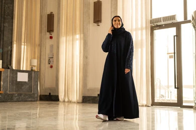 A conversation and chat with friends, a Saudi Arabian Gulf woman in a hijab talking on a mobile phone in a hotel, enjoying time exchanging news and talks, making a phone call, facial expressions indicating happiness and joy.