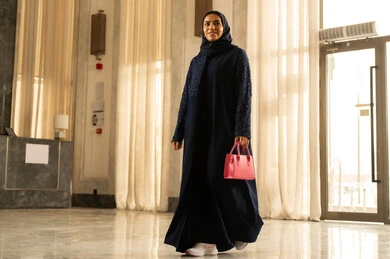 Spending time during the vacation, hotels and resorts in the Kingdom of Saudi Arabia, enjoying the summer holiday, an Arab Gulf Saudi woman wearing a hijab and an abaya holding a red bag in her hands walking inside the tourist hotel, recreational summer trips.