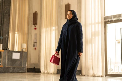 الفنادق والمنتجعات في المملكة العربيه السعودية، الاستمتاع بالعطلة الصيفية , قضاء الأوقات في الإجازة ، امراه عربيه خليجيه سعودية محجبة ترتدي العباءة تمسك بيديها حقيبة حمراء تمشي داخل الفندق السياحي، رحلات الصيف الترفيهية