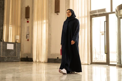 الاستمتاع بالعطلة الصيفية, الفنادق والمنتجعات في المملكة العربيه السعودية , قضاء الأوقات في الإجازة ، امراه عربيه خليجيه سعودية محجبة ترتدي العباءة تمسك بيديها حقيبة حمراء تمشي داخل الفندق السياحي، رحلات الصيف الترفيهية