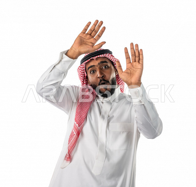 بورتريه لرجل عربي خليجي سعودي ، يرتدي الزي السعودي التقليدي ، بإيماءات وجه ويدين مختلفة تدل على الخوف والرعب ، خلفية بيضاء ، مفهوم الذعر ، الرهبة والخوف من شيء ، حركة اليدين تدل على الابتعاد والتصدي لشيء ما