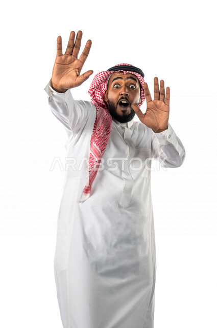 بورتريه لرجل عربي خليجي سعودي ، يرتدي الزي السعودي التقليدي ، بإيماءات وجه ويدين مختلفة تدل على الخوف والرعب ، خلفية بيضاء ، مفهوم الذعر ، الرهبة والخوف من شيء ، حركة اليدين تدل على الابتعاد والتصدي لشيء ما