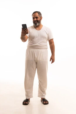التسوق الالكتروني وتصفح برامج وتطبيقات الجوال، الدردشة مع الأهل والأصدقاء، بورتريه لرجل عربي خليجي سعودي يرتدي سروال وفنيله بيضاء يحمل الهاتف المحمول، تطور التكنولوجيا والأجهزة التقنية، صورة الجسم بالطول الكامل، خلفية بيضاء