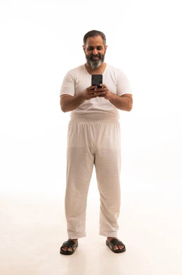 الدردشة مع الأهل والأصدقاء، التسوق الالكتروني وتصفح برامج وتطبيقات الجوال،بورتريه لرجل عربي خليجي سعودي يرتدي سروال وفنيله بيضاء يحمل الهاتف المحمول، تطور التكنولوجيا والأجهزة التقنية، صورة الجسم بالطول الكامل، خلفية بيضاء