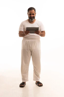 المحادثة مع الأهل والأصدقاء، تصفح مواقع التواصل الاجتماعي عبر الجهاز اللوحي، استعمال التكنولوجيا والتقنية الحديثة، بورتريه لرجل عربي خليجي سعودي يرتدي سروال وفنيله بيضاء يحمل بيده جهاز التابلت، الطول الكامل للجسم، خلفية بيضاء