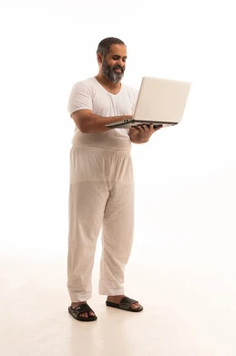 مفهوم العمل عن بعد، انجاز الأعمال من المنزل عبر الانترنت، تصفح برامج و تطبيقات الابتوب، بورتريه لرجل عربي سعودي خليجي يرتدي سروال وفانيلا أبيض يقوم باستخدام اللابتوب، الأجهزة والتقنيات المتطورة، صورة لكامل الجسم، خلفية بيضاء