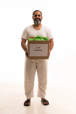 تأمين الملابس وإهدائها للمحتاجين، مفهوم المساعدة والتبرع،  بورتريه لرجل عربي سعودي خليجي يرتدي سروال وفانيلا أبيض يحمل صندوق من الثياب ينظر إلى الكاميرا بإيماءات السرور، توفير المستلزمات الضرورية للفقراء، جمعية خيرية ومبادرة انسانية ، خلفية بيضاء
