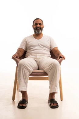 ايماءات الثقة بالنفس، مفهوم القوة والرجولة ، بورتريه لرجل عربي سعودي خليجي يرتدي سروال وفانيلا أبيض يجلس على كرسي  ينظر الى الكاميرا  بتعابير السعادة والسرور، خلفية بيضاء