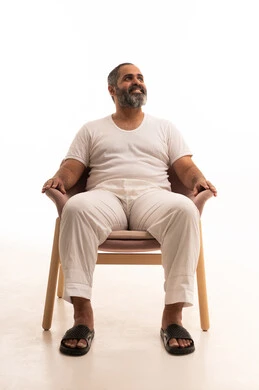 The concept of strength and masculinity, a portrait of an Arab Saudi Gulf man wearing white pants and a t-shirt sitting on a chair looking up somewhere with expressions of contemplation, reflection, and joy, gestures of self-confidence, white background.