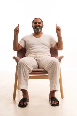 Raising both hands upwards in gestures of an oath, a portrait of an Arab Saudi Gulf man wearing white pants and a t-shirt sitting on a chair, pointing with his index fingers upwards in gestures of testimony and swearing an oath, with a white background.