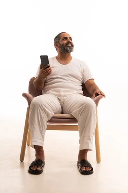 استخدام التطبيقات الحديثة و التسويق الألكتروني, بورتريه لرجل عربي سعودي خليجي يرتدي سروال وفانيلا أبيض يجلس على كرسي يستخدم الجوال, برامج التواصل الاجتماعي عبر الهاتف المحمول, خلفية بيضاء