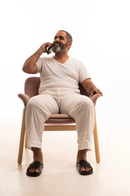 الرد على الاتصالات والمكالمات، التواصل مع الأصدقاء والاقارب، استخدام التقنيات الحديثة المتطورة، سماع أخبار سعيدة عبر الهاتف المحمول، بورتريه لرجل عربي سعودي خليجي يرتدي سروال وفانيلا أبيض يجلس على كرسي يقوم بإجراء مكالمة هاتفية بايماءات السعاده، خلفيه بيضاء