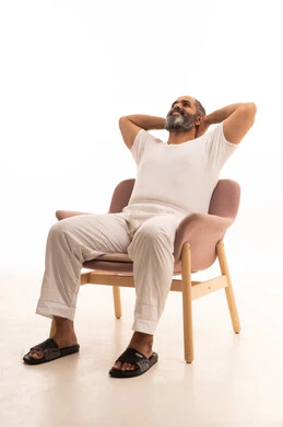 الشعور بالتعب والحاجة إلى النوم، ايماءات تدل على الراحة، مفهوم الاسترخاء والاستمتاع بالأجواء الهادئة، بورتريه لرجل عربي سعودي خليجي يرتدي سروال وفانيلا أبيض يجلس على كرسي ويضع يديه تحت رأسه، خلفية بيضاء