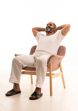 ايماءات تدل على الراحة، مفهوم الاسترخاء والاستمتاع بالأجواء الهادئة، بورتريه لرجل عربي سعودي خليجي يرتدي سروال وفانيلا أبيض يجلس على كرسي ويضع يديه تحت رأسه، الشعور بالتعب والحاجة إلى النوم، خلفية بيضاء