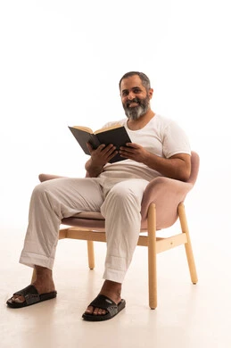 هواية القراءة والاستكشاف، مفهوم التثقيف والبحث العلمي، قضاء وقت الفراغ بالتعلم والثقافة، بورتريه لرجل عربي سعودي خليجي يرتدي سروال وفانيلا أبيض يجلس على كرسي يقرأ كتاب، خلفية بيضاء